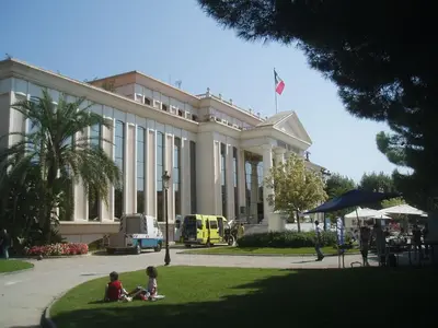 three people sitting in the grass in front of a building at Appartement spacieux & vue imprenable in Saint-Laurent-du-Var