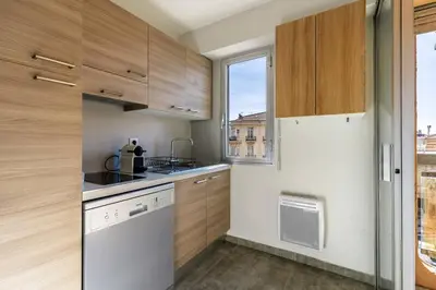 a small kitchen with wooden cabinets and a window at Jolie studio avec belle terrasse ensoleillee in Nice