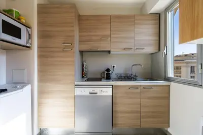 a kitchen with wooden cabinets and a white dishwasher at Jolie studio avec belle terrasse ensoleillee in Nice