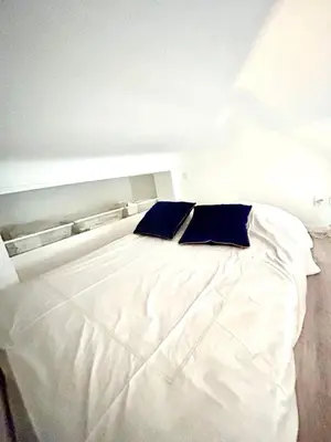 a white bed with two blue pillows on it at City Center Studio - 1 min Train Station & Main Street in Nice