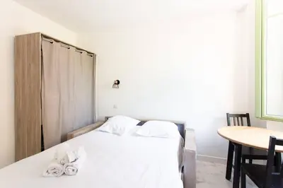 a bedroom with a bed with white sheets and a table at LYMPIA -Cosy studio, 200 m plages de Nice - Le Port in Nice