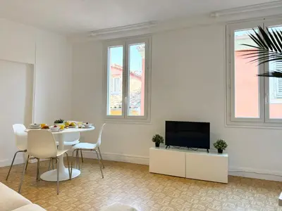 a white living room with a table and a tv at Charmant 2 pièces proche mer in Nice