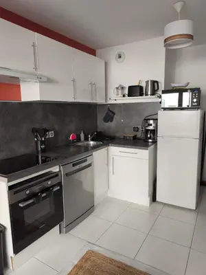 a kitchen with white cabinets and black appliances at Studio calme et paisible, climatisé avec terrasse au dernier étage, 100m du tramway et 20 min de la promenade des anglais in Nice