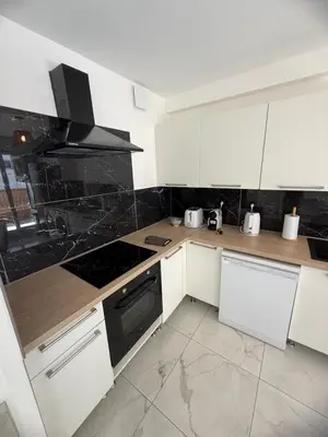 a kitchen with white cabinets and black appliances at Magnifique 3 pièces à 100m de la mer in Nice