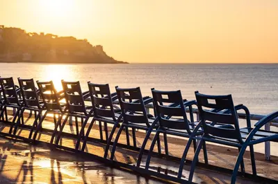 a row of chairs on the beach at sunset at Charming flat, fully equipped, air conditioning, beach only 300m - LA LOGE in Nice