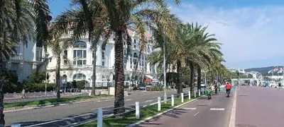a man riding a bike down a street with palm trees at Appartement vue mer et panoramique, 2 chambres, 3 lits in Nice