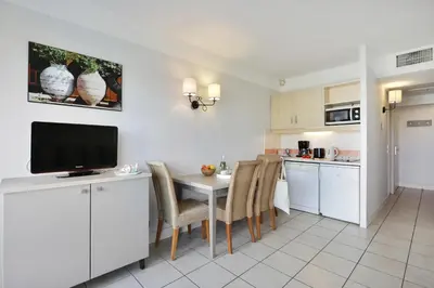 a kitchen with a table with chairs and a television at Résidence Héliotel Marine in Saint-Laurent-du-Var