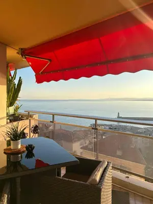 a red umbrella on a balcony with a table and chairs at Magnifique appartement - Vue mer in Nice