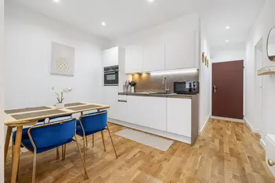 a kitchen with white cabinets and a table and blue chairs at Nice Renting - 5 Massena - Elegant Air-Conditioned Cocoon Quiet Patio Massena in Nice