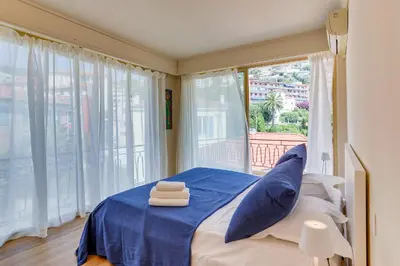 a bedroom with a bed with blue sheets and a window at Dina palace AP4462 By Riviera Holiday Homes in Villefranche-sur-Mer