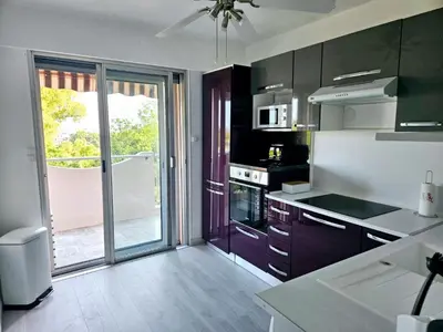 a kitchen with black cabinets and a large sliding glass door at T2 Vue Mer avec Grande Terrasse & Parking 4 min Plage - SpiritofFamily06 in Cagnes-sur-Mer