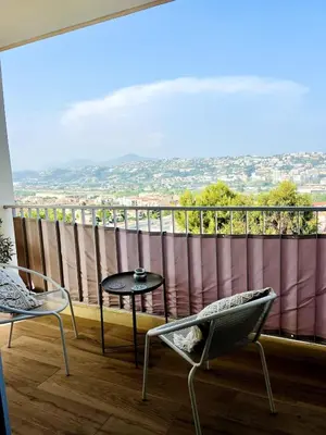 a balcony with a table and chairs and a large window at Lea's cozy nest with a sea-mountain view in Saint-Laurent-du-Var