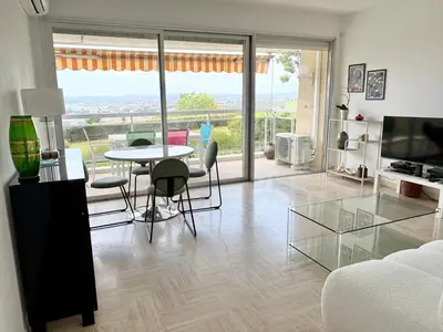 a living room with a table and chairs and a large window at Quiet Flat with view and Swimming pool in Nice