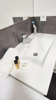 a white bathroom sink with a person in a white glove at T4 avec grande terrasse - BBQ - parking in La Trinité