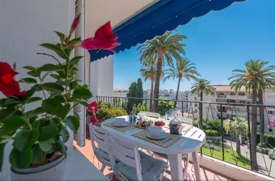 a table and chairs on a balcony with palm trees at Beaulieu Garden Apartment in Beaulieu-sur-Mer