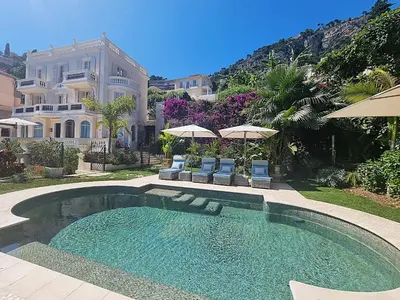 a swimming pool with chairs and umbrellas in front of a house at Villa Soleil Riviera in Villefranche-sur-Mer