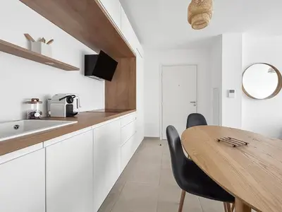 a kitchen with white cabinets and a wooden table at Spacieux T2 à 150m Des Plages in Cagnes-sur-Mer