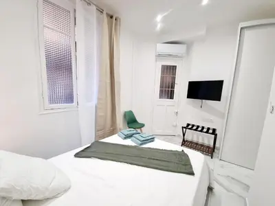a white bedroom with a bed and a green chair at Spacious Family Apartment Near Sea - Nice in Nice