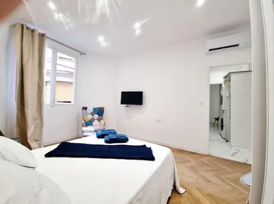 a white bedroom with a bed and a tv on the wall at Spacious Family Apartment Near Sea - Nice in Nice