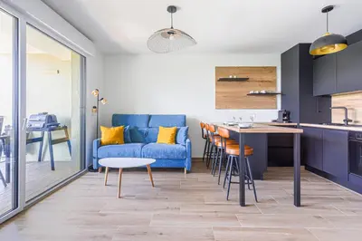 a living room with a blue couch and a kitchen at Ciel d'Azur - Climatisé piscine partagée in Saint-Laurent-du-Var