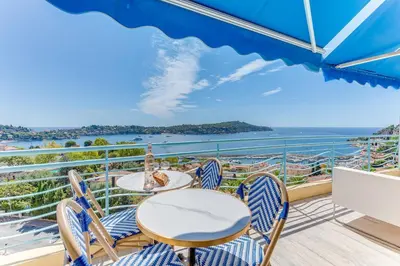 a balcony with a table and chairs and a view of the water at PANORAMIC ESTEREL AP4475 By Riviera Holiday Homes in Villefranche-sur-Mer