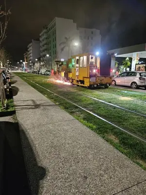 a train on tracks next to a sidewalk at night at T1 Bord De Mer Nice West in Nice