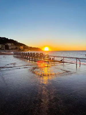 a beach with the sun rising over the ocean at L'Embarcadère - Port de Nice in Nice