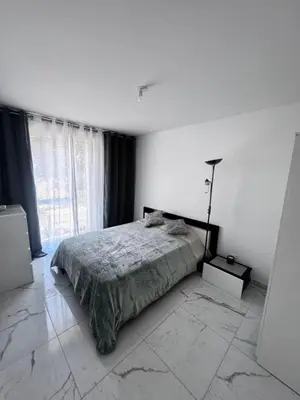 a white bedroom with a bed and a large window at Luxueux appartement climatisé avec piscine & parking in Saint-Laurent-du-Var