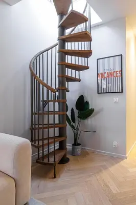 a wooden spiral staircase in a living room with a plant at Wide Open Sky Terrace 1 Bdr in Nice