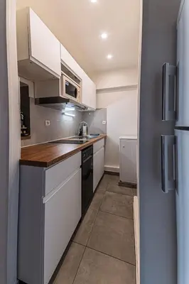 a small kitchen with white cabinets and a refrigerator at Studio rénové à deux pas de la mer et commerces in Cagnes-sur-Mer