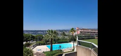 a view of a swimming pool with palm trees and a building at Lovely apartment with private garden and a swimming-pool in Nice
