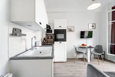a white kitchen with a sink and a table at Appartement Perle - Welkeys in Nice
