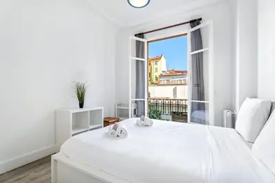 a white bedroom with a white bed and a window at Appartement Perle - Welkeys in Nice