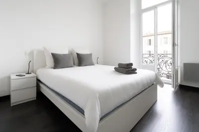 a white bedroom with a white bed and a window at Le Malausséna in Nice