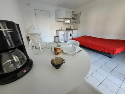a kitchen with a white table and a red bed at Studio climatisation balcon à 5 min de la plage in Nice