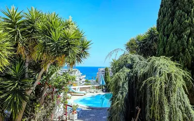 a resort with a pool and palm trees and the ocean at Villa le Mazet, Nice, piscine, vue mer, Promenade des Anglais, Baie des Anges in Nice