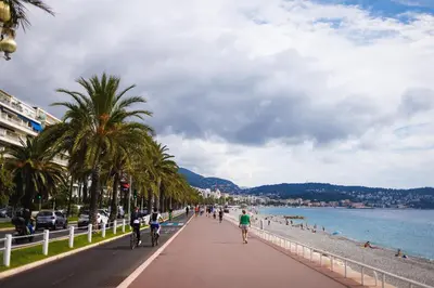 a group of people riding bikes down a sidewalk next to the beach at Plage et Salsa, Nice Promenade des anglais in Nice