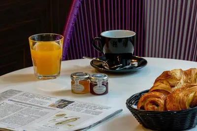 a table with a cup of orange juice and a basket of pastries at Hôtel & Appartements Monsigny in Nice