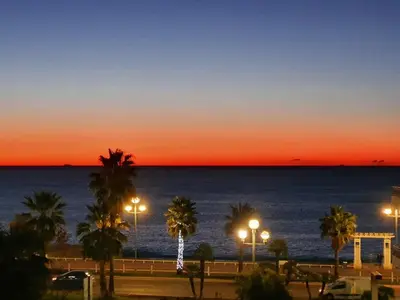 a sunset over the ocean with palm trees and lights at Sea View, Modern Apartment and Terrace in Nice
