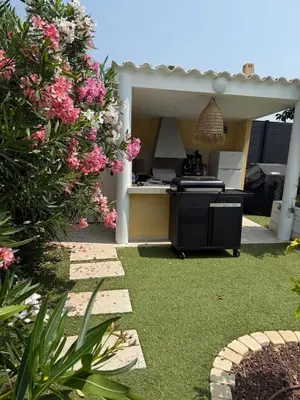 a backyard with a kitchen and a garden with pink flowers at Charmant appartement, piscine 15 min de Nice in Carros