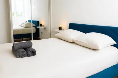 a white bed with a blue headboard and a mirror at Appartement confortable avec balcon - Proche Gare Riquier SNCF in Nice