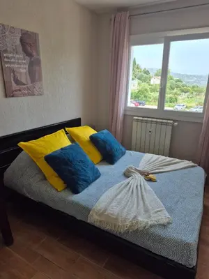 a bed with blue and yellow pillows and a window at F2 vue mer et montagne au calme in Nice