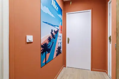a hallway with an orange wall with a poster of a hotel at 44 LAMARTINE - Charmant 2 pieces - Centre-ville in Nice