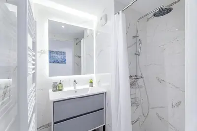 a white bathroom with a sink and a shower at Appartement Colombier - Welkeys in Saint-Laurent-du-Var