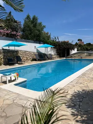 a large swimming pool with blue umbrellas and chairs at Appartement dans villa vue mer piscine partagée in Saint-Laurent-du-Var