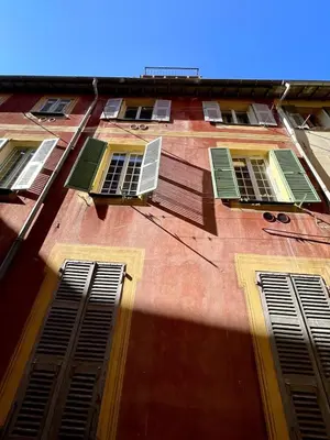 a tall red brick building with green shuttered windows at Studio Vieux-Nice proche de la mer et Cours Saleya in Nice