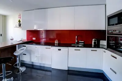 a kitchen with white cabinets and a red wall at Appartement luxueux entier 3 chambres in Nice