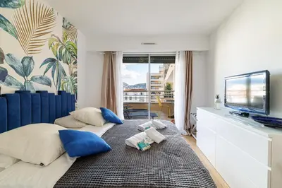 a bedroom with a bed with blue pillows and a tv at MY CASA - PALAIS MED 702 D - 2 bedroom Down Town with Terasse AC in Nice