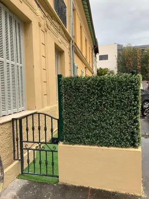 a green hedge next to a building with a gate at Élégant T2 au calme in Nice