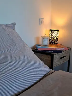 a bed with a nightstand with a book and a alarm clock at Studio de la Villa Thérèse, Piscine & Jardin in Saint-Laurent-du-Var
